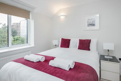 a white bedroom with a large white bed with red pillows at Roomspace Serviced Apartments - Nevis Court in Surbiton