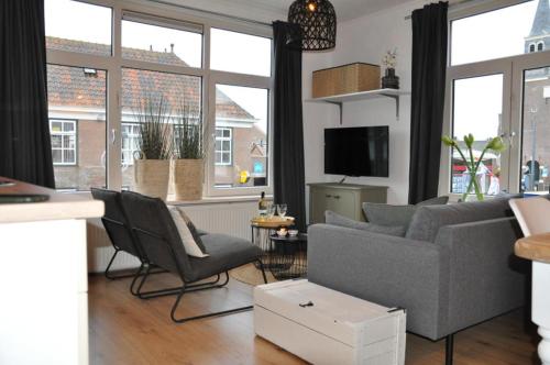 een woonkamer met een bank, stoelen en ramen bij Sunny Reef in Egmond aan Zee