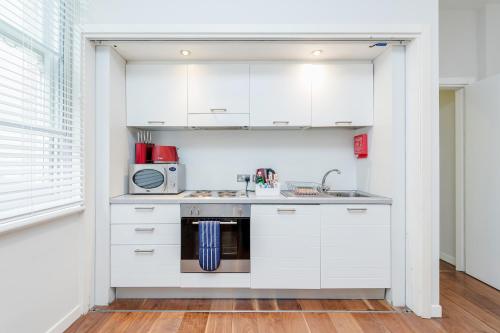 ロンドンにあるRoomspace Serviced Apartments - Sterling Houseの白いキャビネットとシンク付きのキッチン