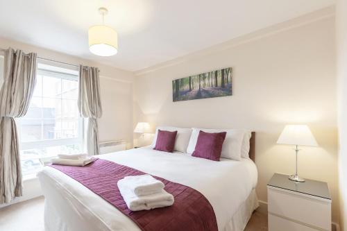 a bedroom with a large white bed with purple pillows at Roomspace Serviced Apartments - Central Walk in Epsom