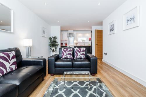 a living room with two black leather couches and a kitchen at Roomspace Serviced Apartments - Abbot's Yard in Guildford