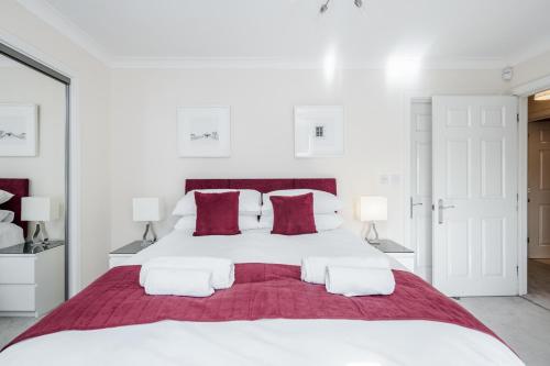 um quarto branco com uma grande cama branca com almofadas vermelhas em Roomspace Serviced Apartments - Royal Swan Quarter em Leatherhead