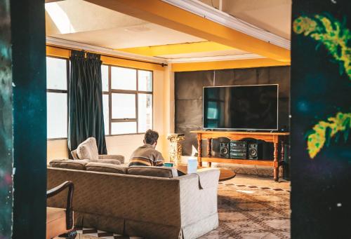 a man sitting on a couch in a living room with a television at The Rooftop Bolivia in La Paz