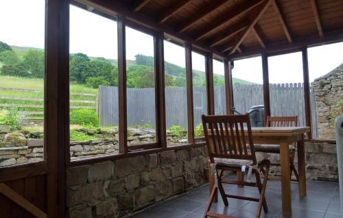 eine Veranda mit einem Holztisch, Stühlen und Fenstern in der Unterkunft East Lane Barn in Aysgarth