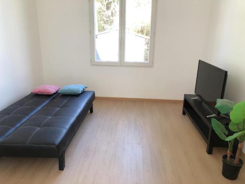 ein Wohnzimmer mit einem schwarzen Sofa und einem Flachbild-TV in der Unterkunft petite maison avec jardin dans banlieue de Paris in Cormeilles-en-Parisis