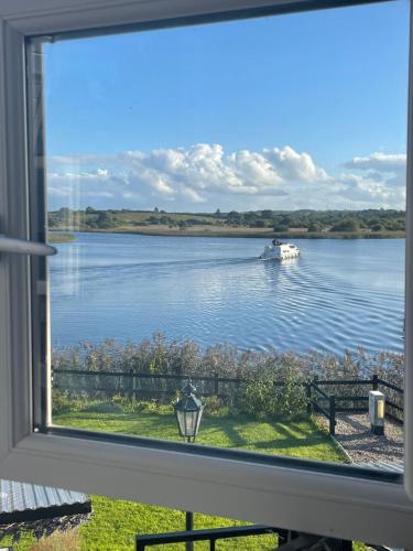 a window with a view of a boat in the water at Lough Key Luxury Riverfront Apartment in Cootehall