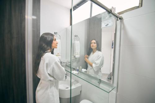 Bianco Hotel Boutique في كوكوتا: امرأة تنظر إلى انعكاساتها في مرآة الحمام