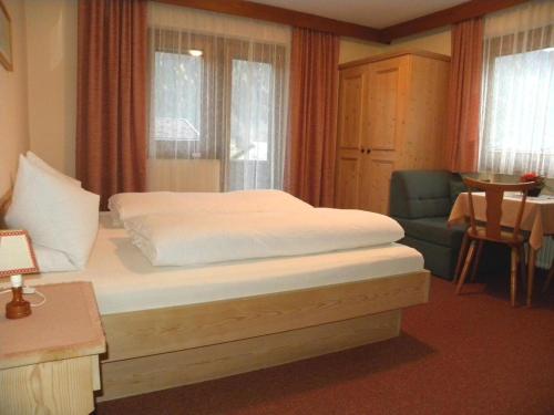 a bedroom with a bed and a chair and windows at Gästehaus Emberger in Mayrhofen