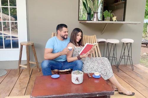 a man and woman sitting on a bench reading a book at Wabi Sabi , casa de playa in Tamanique