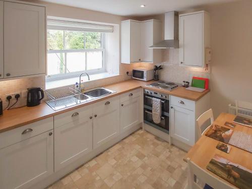 a kitchen with white cabinets and a sink and a window at Uk35715 - South Cottage in Teviothead