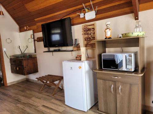 a kitchen with a microwave and a refrigerator and a tv at Chale Vale Encantado in São Bento do Sapucaí