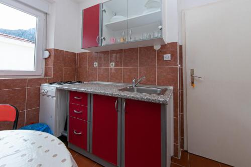 una cucina con armadi rossi, lavandino e finestra di Apartments with a parking space Gradac, Makarska - 5198 a Gradac (Grado)