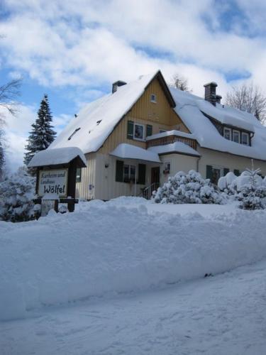 a house covered in snow with a sign in front at Pension Wölfel in Bad Steben