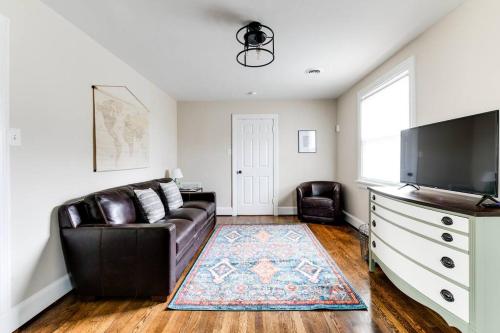 a living room with a leather couch and a flat screen tv at RVA Cottage Cozy & Spacious Near Downtown in Richmond