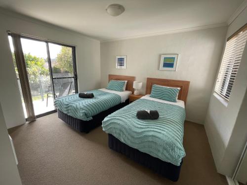 two beds in a room with a window at Seachange Apartments Merimbula in Merimbula