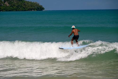 a man riding a wave on a surfboard in the ocean at Arinara Beach Resort Phuket - SHA Extra Plus in Bang Tao Beach