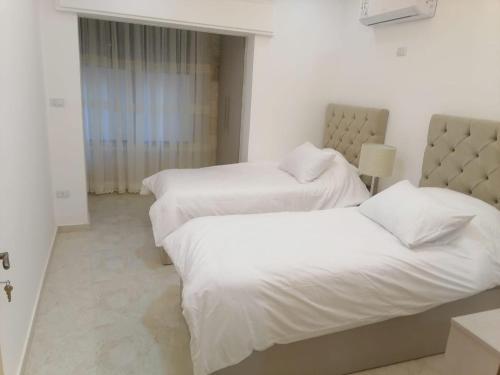 two beds in a hotel room with white sheets at Executive Apartments in Amman