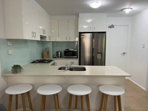 een keuken met witte kasten en een aanrecht met 4 krukken bij 2 bedroom modern coastal retreat in Kiama