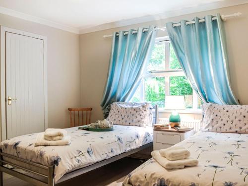 a bedroom with two beds and a window with blue curtains at Corrennie School Cottage in Whitehouse