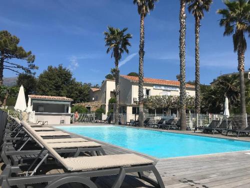 a swimming pool with chaise lounge chairs and palm trees at Hôtel Restaurant Les Chasseurs in Marine de Pietracorbara