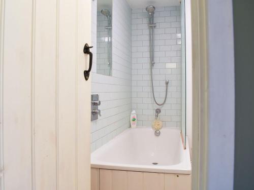 La salle de bains blanche est pourvue d'une baignoire et d'une douche. dans l'établissement St James Cottage, à Shaftesbury