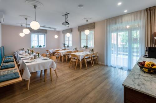 restauracja z białymi stołami, krzesłami i oknami w obiekcie Ditlin Apartmanok w mieście Pápa