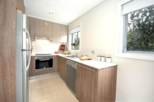 una cocina con armarios de madera y una gran ventana en VELLY-Modern Light 2BR Moments from Clovelly Beach, en Sídney