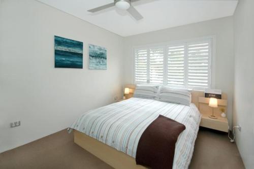 a white bedroom with a bed and a window at VELLY-Modern Light 2BR Moments from Clovelly Beach in Sydney