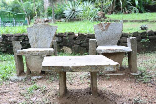 two stone chairs and a bench next to a stone wall at Ella Planters Bungalow in Ella