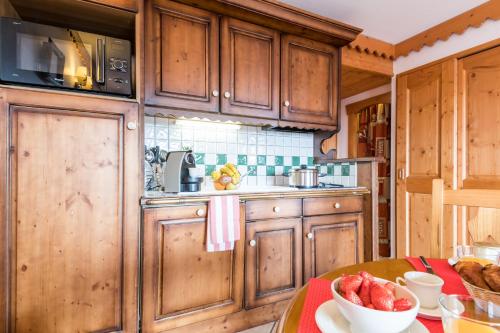 a kitchen with wooden cabinets and a table with a bowl of fruit at Résidence Pierre & Vacances Premium Le Roselend in Arc 1800