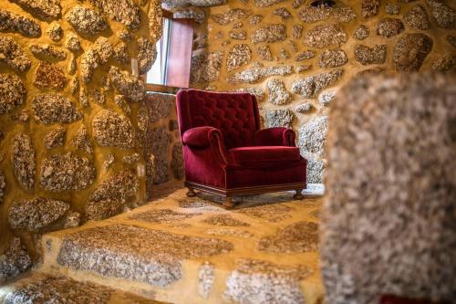 a red chair sitting in a room with a stone wall at Gerês Country Stays - Lagar in Rio Caldo