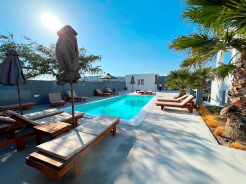 a swimming pool with chaise lounge chairs and an umbrella at White Lily Santorini - Adults Only 16 Plus in Perivolos