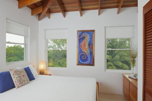 a bedroom with a bed and three windows at Weezie's Ocean Front Hotel and Garden Cottages in Caye Caulker