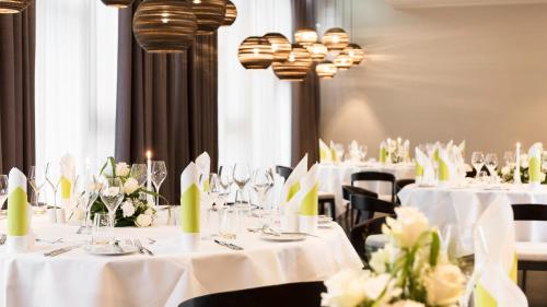 a dining room with white tables and chairs with flowers at Holiday Inn Dresden - Am Zwinger by IHG in Dresden