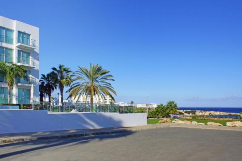a street in front of a building with palm trees and the ocean at Lucile - Coralli Beachfront Apartment in Paralimni