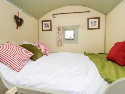 um quarto com uma cama branca com almofadas vermelhas e verdes em Sweet Briar Shepherds Hut em Brecon