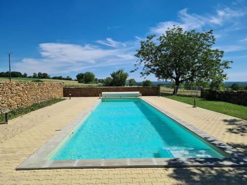 a swimming pool with blue water in front of a stone wall at Maison chaleureuse près de Rocamadour in Alvignac