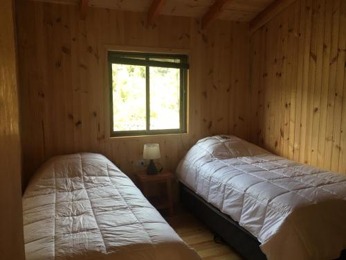 2 camas en una cabaña de madera con ventana en Los Quenes River Lodge, en Los Queñes