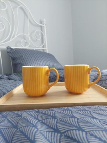 two orange cups sitting on a wooden tray on a bed at Pigeon apartment in Kuldīga