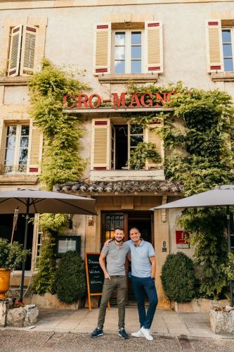 two men are standing in front of a restaurant at Hôtel Le Cro-Magnon in Les Eyzies-de-Tayac