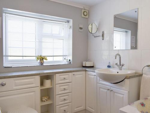 uma casa de banho branca com um lavatório e uma janela em September Cottage em Chickerell