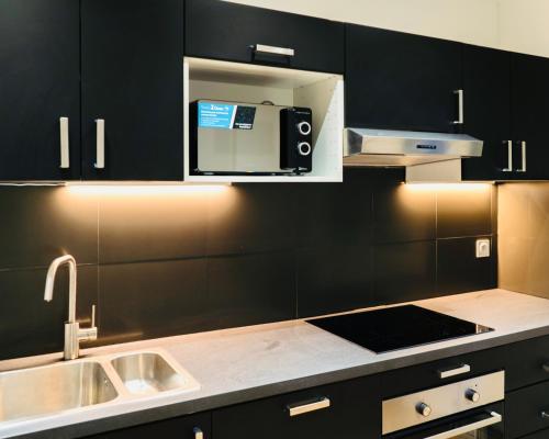 La cuisine est équipée de placards noirs, d'un évier et d'un four micro-ondes. dans l'établissement Bella Luna III - Elégant appartement centre ville - Parking gratuit - Wifi ultra rapide-Appareil Massage-Netflix-Jeu société, à Troyes