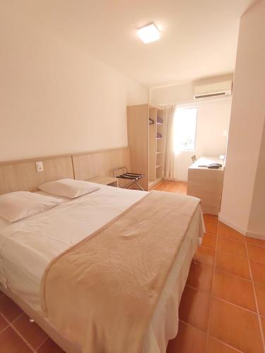 a bedroom with a large white bed and a desk at Avenida Palace Hotel in Joinville