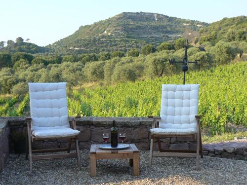two white chairs and a table with a bottle of wine at Pessighette Dimora Di Campagna in Bosa