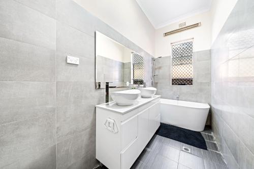a white bathroom with two sinks and a bath tub at 4 Bedroom house 500M to Drummoyne Bay Run in Sydney