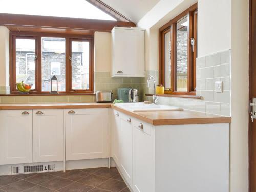 uma cozinha com armários brancos, um lavatório e janelas em Campbell Cottage em Windermere