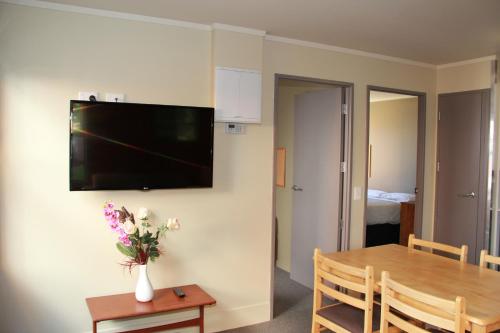 a dining room with a table and a television on a wall at Nikau Apartments in Nelson
