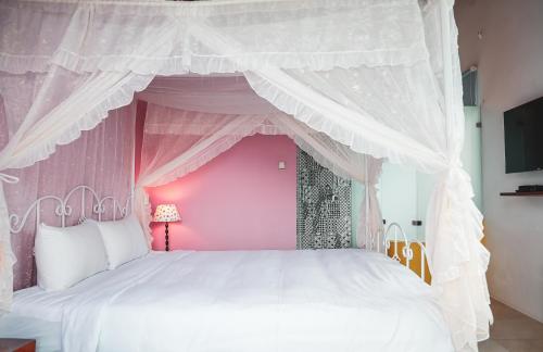 ein rosafarbenes Schlafzimmer mit einem weißen Bett mit Baldachin in der Unterkunft Canaan B&B Kenting in Eluan