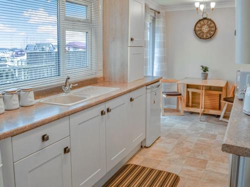 a kitchen with white cabinets and a sink and a window at Mistlethrush in Horning