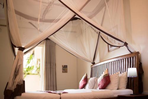 een slaapkamer met een hemelbed met kussens en een raam bij Entebbe Palm Hotel in Entebbe
